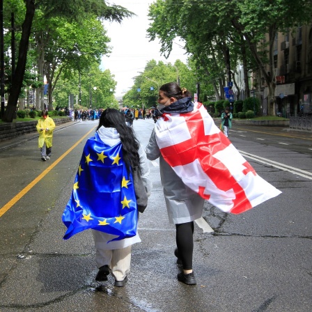 Zwei Demonstranten haben sich die georgische und die EU-Flagge umgebunden und laufen damit eine Straße in Tiflis entlang.