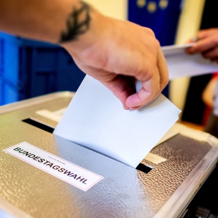 Hand steckt Wahlzettel in Urne mit der Aufschrift 'Bundestagswahl'.