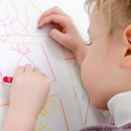 Ein kleines Mädchen malt mit der linken Hand ein Bild.