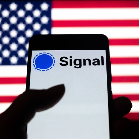 Foto-Illustration zeigt ein Logo der Signal-App auf einem Smartphone-Bildschirm mit einer US-Flagge im Hintergrund 