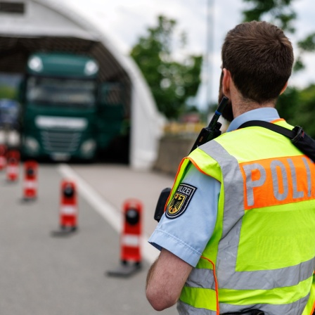 Ein Polizist sichert an der deutschen Grenze die Kontrollstelle auf einer Raststätte, in der ein gestoppter Lastwagen steht.