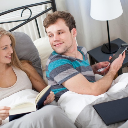 Symbolbild: Frau mit Buch und Mann mit Handy im Bett