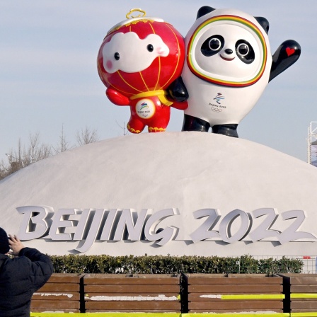 Ein Mann fotografiert die olympischen Maskottchen Panda Bing Dwen (r/Olympia) und Shuey Rhon Rhon (Paralympischen Winterspiele 2022). Im Hintergrund ist der Oympiaturm zu sehen.