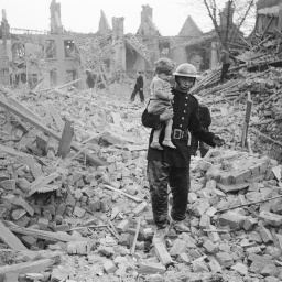 Ein Feuerwehrmann trägt ein Kleinkind nach einem Bombenangriff aus den Trümmern, London, um 1940. 