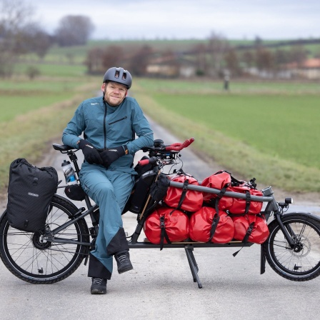 Ein Mann schaut von seinem vollgepackten Lastenrad in die Kamera