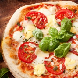 Symbolbild einer Pizza mit Tomaten, Mozarella und Basilikum.