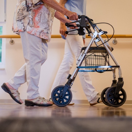 Eine Pflegekraft geht in einem Pflegeheim mit einer älteren Dame über einen Korridor.