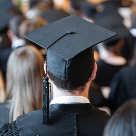 Absolventen der Universität Mannheim tragen während der Abschlussfeier in der Aula Absolventenhüte.