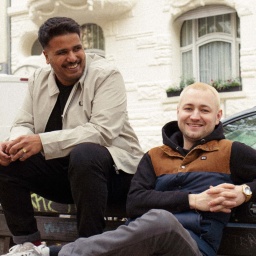 Das Produzenten-Duo Indialman auf einer Bank an einer Straße sitzend