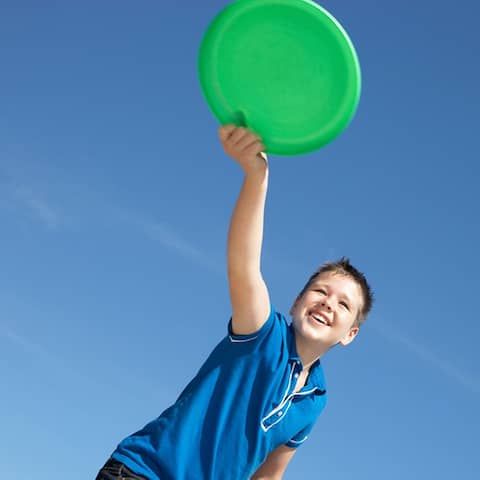 Ein Junge wirft eine grüne Frisbeescheibe.