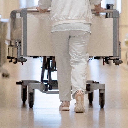 Eine Krankenpflegerin schiebt ein Krankenbett durch einen Flur. 