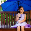 Ein Mädchen sitzt auf einer Bank unter einem großen Regenschirm