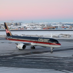 Ein Flugzeug mit dem Schriftzug "Trump" landet auf dem Flughafen von Nuuk. Im Hintergrund sind die verschneite Stadt und der Fjord zu sehen.