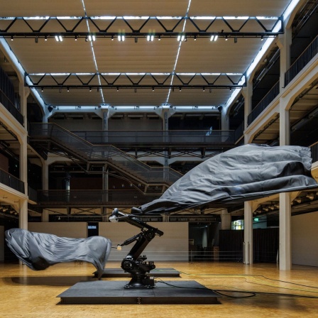 Zwei Industrieroboter mit schwarzen Flaggen führen eine komplexe und kontrapunktische Choreografie aus