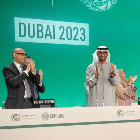 COP-Präsident Al Jaber steht klatschend auf dem Podium zum Abschluss der Weltklimakonferenz 2023 in Dubai. 