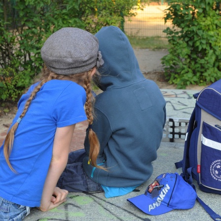 Zwei Kinder mit Schulranzen auf dem Spielplatz