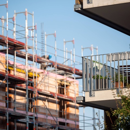 Ein Gerüst steht an der Baustelle eines Neubaus. Neben der Baustelle steht ein bereits fertiggestellter Neubau.