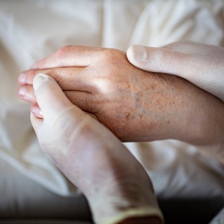 Die Hand eines älteren Menschen wird von zwei Händen in medizinischen Handschuhen gehalten (Bild: picture alliance / Ute Grabowsky)