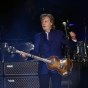 Ein Mann mit Gitarre steht auf einer Bühne. Er trägt eine dunkelblaue Jacke. Es ist der frühere Beatle Paul McCartney.