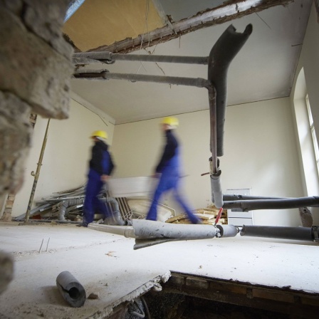 Zwei Bauarbeiter tragen eine Metallwanne bei der Sanierung eines Altbaus. © IMAGO / photothek / Thomas Koehler 