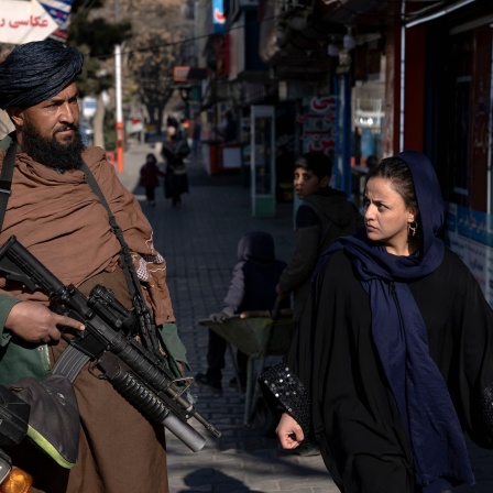 Ein Taliban-Kämpfer steht Wache, während eine Frau vorbeiläuft