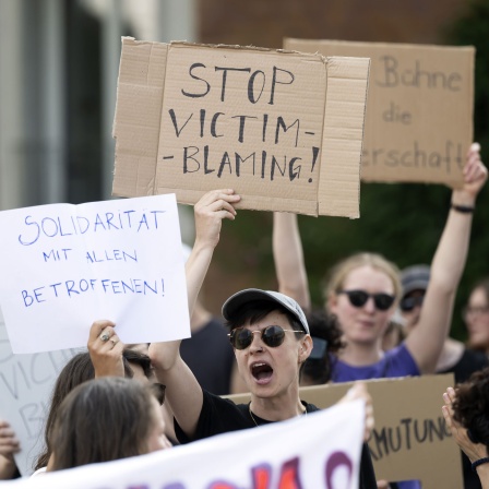 Menschen demonstrieren gegen einen Auftritt von Rammstein und halten Plakate mit der Aufschrift "Stop victim blaming" und "Solidarität mit allen Betroffenen" hoch.