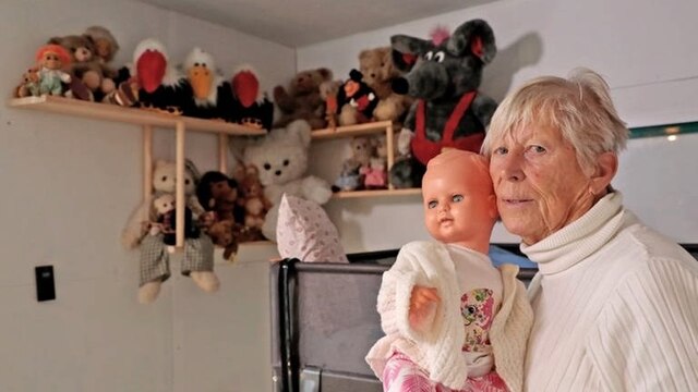 Inge Behrendt und ihre Puppe Eugen, im Hintergrund Stofftiere auf Regalen
