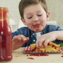 Ein Junge isst Pommes mit Ketchup