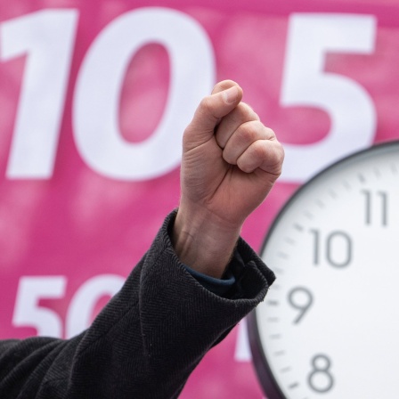 Ein Streikender ballt eine Faust, im HIntergrund ist die Forderung nach 10,5 Prozent mehr Lohn zu sehen und eine Uhr, die 5 nach 12 anzeigt. (Bild: Marijan Murat/dpa) 