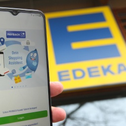 Ein Mann hält vor einer Filiale von Edeka ein Smartphone in der Hand, auf dem die App von Payback aufgerufen wurde. Ab 2025 kooperieren Edeka und das Bonuspunkte-Programm.