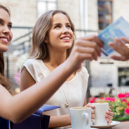 Zwei Freundinnen in einem Café, eine bezahlt mit einem Geldschein