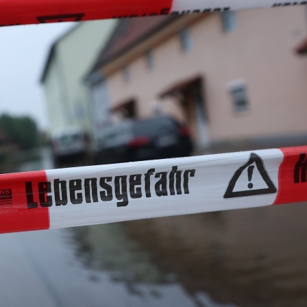 "Lebensgefahr" ist auf einem Absperrband vor einer von der Mindel überfluteten Straße zu lesen. © picture alliance/dpa/Karl-Josef Hildenbrand