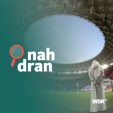 Mann mit traditioneller Kleidung steht in Fuball-Stadion in Katar. Daneben das Podcast-Logo: Schriftzug "nah dran", daneben eine kleine Lupe.