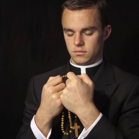 Junger Priester mit geschlossenen Augen, in den Händen einen Rosenkranz.