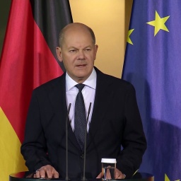 Bundeskanzler Olaf Scholz (SPD) am Rednerpult, im Hintergrund die Nationalflagge und die Europaflagge.