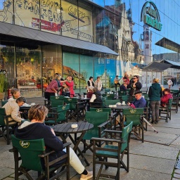 Menschen sitzen im Freien auf dem Marktplatz von Chemnitz in einem Café an Tischen.