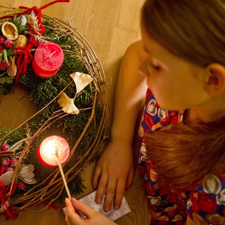 Kind zündet Kerze auf einem Adventskranz an