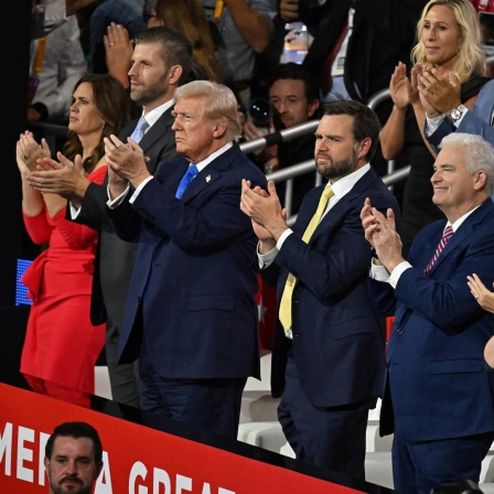 Donald Trump steht mit mehreren Menschen beim Parteitag der Republikaner auf der Tribüne und klatscht. Neben ihm steht J. D. Vance und klatscht ebenfalls. 