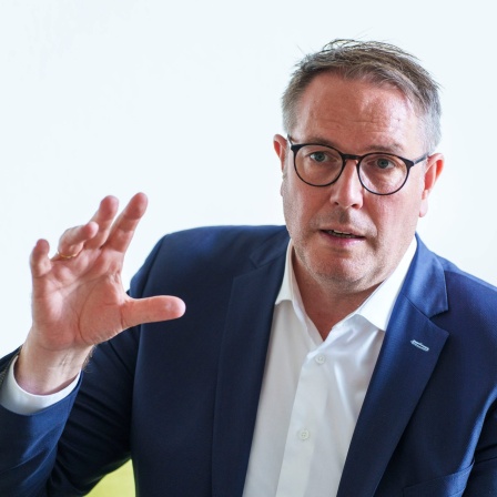 Der rheinland-pfälzische Sozialminister Alexander Schweitzer (SPD) sitzt beim Sommerinterview auf dem &#034;Grünen Sofa&#034; der Deutschen Presse-Agentur in Mainz. Er redet und gestikuliert mit den Händen.