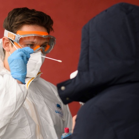 Ein Mitarbeiter nimmt einen Abstrich von einer Patientin für einen PCR-Test auf das Coronavirus vor einer Arztpraxis