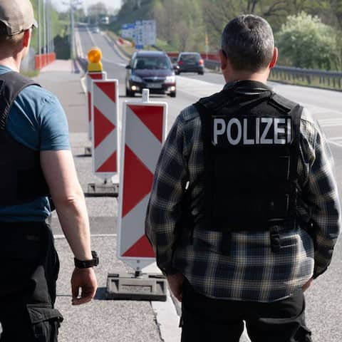 Zwei Polizisten stehen am Grenzübergang am Straßenrand und beobachten den Verkehr.