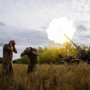 Ukrainische Soldaten feuern an der südlichen Frontlinie der Ukraine am 15. September 2022. Zwei Soldaten gehen in Deckung und halten sich die Ohren zu. Eine Rauchsäule steigt auf.