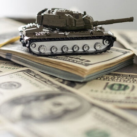 Ein Miniatur bzw. Spielzeug-Panzerfahrzeug fährt über Dollar-Scheine hinweg
