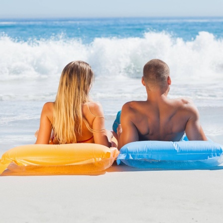 Eine Frau und ein Mann auf Luftmatratzen beim Sonnenbad am Strand: Bräune entsteht durch ein bestimmtes Farbpigment, das Melanin heißt. Es bildet sich unter der Haut, wenn UV-Strahlung auf die Hautzellen kommt. Diese UV-Strahlung, vor allem die UV-B-Strahlung, produziert das Melanin.
