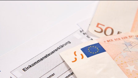 Das Formular der Einkommensteuererklärung und zwei 50-Euro-Scheine liegen auf einem Tisch