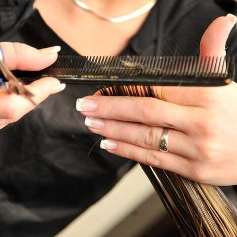 Frau schneidet Haarsträhne mit Schere und Kamm