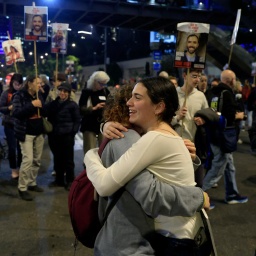 Menschen reagieren erfreut über die Meldung einer möglichen Waffenruhe und umarmen sich auf einer Demo in Tel Aviv. 