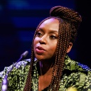 Chimamanda Ngozi Adichie spricht in ein Mikrofon und unterstreicht ihre Worte mit einer zupackenden Geste.