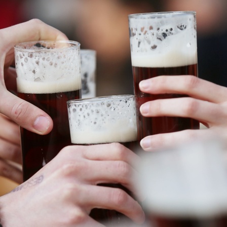 Die Hände von vier Personen beim Anstoßen mit Biergläsern
