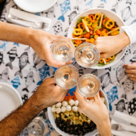 Ein Tisch einer Wohngemeimschaft beim gemeinsamen Essen, die Gläser prosten sich in der Mitte zu.